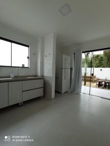 a white kitchen with a refrigerator and a large window at Casa geminada 2 no Mariscal in Bombinhas