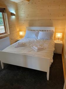 a white bed in a wooden room with two lamps at Hulver Lodge, Snape, Suffolk. in Snape