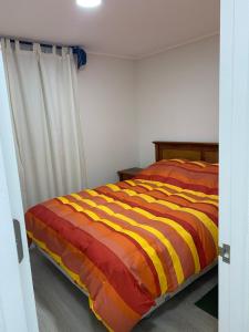 - un lit avec une couette à rayures orange et jaune dans la chambre dans l'établissement Hermoso Departamento familiar en condominio, à El Tabo