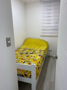 a small bedroom with a bed with a yellow comforter at Hermoso Departamento familiar en condominio in El Tabo
