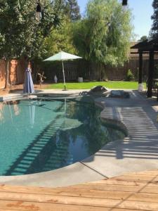 een vrouw die naast een zwembad met een parasol staat bij Clovis, CA National Parks Room in Clovis