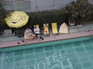 two people sitting in chairs next to a pool with an umbrella at Josh Hotel in Bangkok