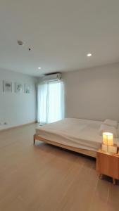 Cozy 1-bedroom condo close to MRT near JJ market في Bang Su: غرفة بيضاء مع سرير وطاولة مع مصباح