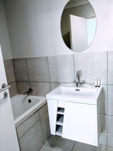 a white bathroom with a sink and a mirror at On The Beach at Surfers Corner in Cape Town