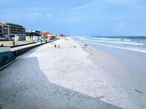 a beach with people walking on the sand and the ocean at On The Beach at Surfers Corner in Cape Town