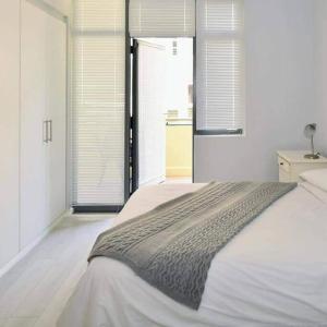 a white bedroom with a bed and a window at On The Beach at Surfers Corner in Cape Town