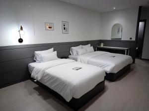 two beds in a hotel room with white sheets at Hi& Hotel in Pyeongtaek