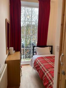 1 dormitorio con 1 cama con cortinas rojas y ventana en 27 Argyle Square en Londres