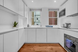 een witte keuken met witte kasten en een houten vloer bij Two Bedroom Serviced Apartment in Artillery Lane in Londen