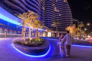 a man and woman walking in front of a building at night at Limassol Del Mar in Limassol