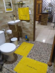 a bathroom with a toilet and two yellow mats on the floor at Borogodó House in Barra Grande