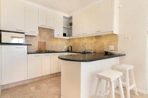 una cocina blanca con armarios y taburetes blancos en Ingleside Luxury apartment by Totalstay, en Ciudad del Cabo