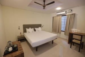 1 dormitorio con 1 cama blanca y ventilador de techo en Elysian Grand Hotel en Bangalore