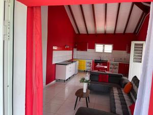 a kitchen with red walls and a living room with a couch at M'LOCATION - La Fontaine Bleue in Le Moule