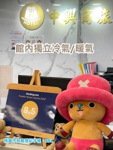 un ours en peluche portant un chapeau rose et une boîte dans l'établissement Jung Shin Hotel, à Zhongli