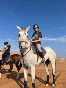 Una mujer montando un caballo blanco en el desierto en Crescent Desert Private Camp en Shāhiq