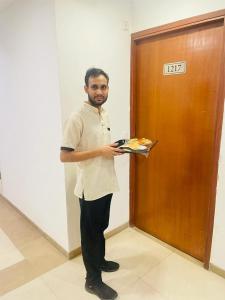 a man standing next to a door holding a tray of food at Maple Tree, Lucknow - Couple Friendly in Lucknow