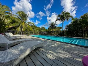 - une piscine avec une terrasse en bois et des chaises à côté dans l'établissement Domaine de la Palmeraie, au Diamant