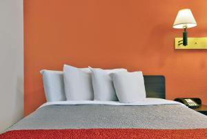 a bed with white pillows in a room with an orange wall at Motel 6-Normal, IL - Bloomington Area in Cardinal Court