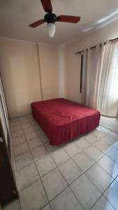 Schlafzimmer mit einem roten Bett und einem Deckenventilator in der Unterkunft 074 Cantinho da Praia - 1 quarto c/ varanda - 200 m da praia - WI FI e com área de lazer - PISCINA e Salão de Jogos e ESTACIONAMENTO GRATUITO in Praia Grande