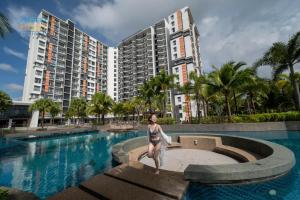 a woman in a bikini standing next to a swimming pool with buildings at Timurbay Beachfront by Perfect Host in Kuantan