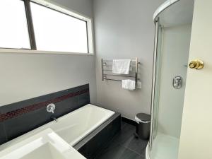 La salle de bains est pourvue d'une baignoire, d'un lavabo et d'une douche. dans l'établissement Central Petone, lovely 4 bedroom, à Lower Hutt