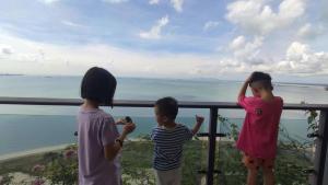 Tres niños parados en un balcón con vistas al océano en 森林城市豪华公寓房, en Kampong Pekajang Bengkok