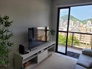 ein Wohnzimmer mit einem TV und einem großen Fenster in der Unterkunft Ótimo apto Enseada Guarujá in Guarujá