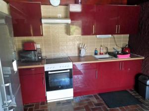 La cuisine est équipée de placards rouges et d'une cuisinière blanche. dans l'établissement The House in the Woods, à Prelauff