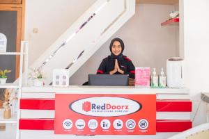 a woman standing behind a red door counter with a laptop at RedDoorz Syariah at Aura Homestay in Ponorogo