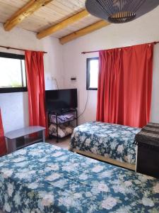 2 camas en una habitación con cortinas rojas en Cabaña Los Algarrobos, en Villa Icho Cruz