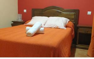 a bed with two white pillows and an orange blanket at Hostal El Hidalgo in Villaluenga