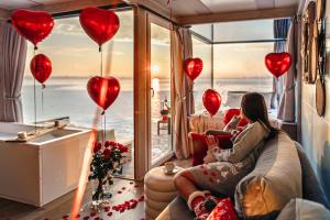 a woman sitting on a couch in a room with heart balloons at Domki na wodzie - HT Houseboats - with sauna, jacuzzi massage chair in Mielno