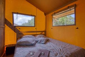 um quarto com uma cama num quarto amarelo com 2 janelas em JOINS! Glamping Aquitaine em Saint-Aigne