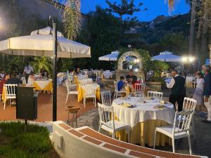 un restaurante con mesas blancas, sillas y sombrillas en Hotel Tirreno, en Parghelia