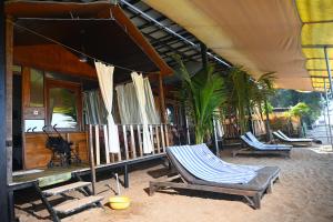 eine Terrasse mit Stühlen und ein Haus mit einer Palme in der Unterkunft Madhu Huts Agonda in Agonda