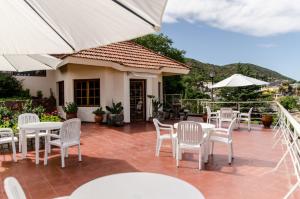 eine Terrasse mit weißen Stühlen, Tischen und einem Sonnenschirm in der Unterkunft del Buen Ayre in Villa Carlos Paz