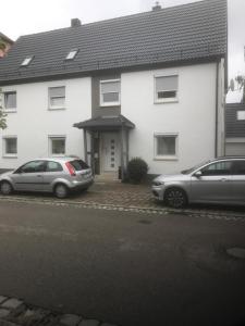 twee auto's geparkeerd voor een wit huis bij Ferienwohnung Romantica EG in Schopfloch
