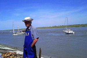 un homme dans un tablier bleu debout à côté de l'eau dans l'établissement AUTHENTIQUE MAISON DE PECHEUR ENTRE-TERRE & MER, à Saint-Valery-sur-Somme