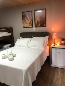 Un dormitorio con una gran cama blanca con dos cuadros en la pared. en Suites da Lu, en Penha