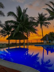 a swimming pool with palm trees and a sunset at HOTEL UTZTZABA in Monterrico