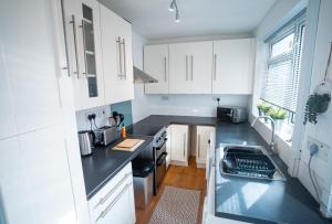 cocina con armarios blancos y encimera negra en Comfortable equipped House in Nuneaton sleeps5 with FREE parking, en Nuneaton