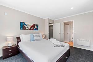a white bedroom with a large bed and a night stand at Tui Lookout - Spa Pool & Lake Views in Taupo