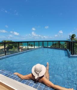 a woman in a hat laying in a swimming pool at Flat La Ursa da Praia in Porto De Galinhas