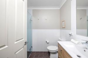 a white bathroom with a toilet and a sink at Aqua Lagoon - Great Family Beach Getaway in Nelson Bay