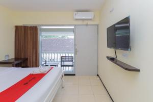 a room with a bed and a tv and a balcony at RedDoorz at CBR Residence Blimbing in Malang