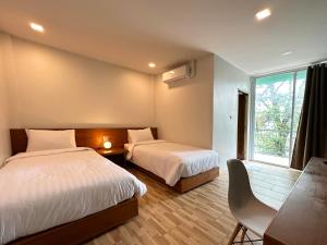 a bedroom with two beds and a desk and a window at Plernpetch Hotel in Suratthani