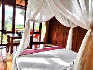 Cette chambre comprend un lit avec des rideaux blancs et une table. dans l'établissement Sang Tirta Resort, à Penebel