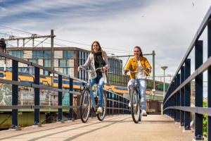 dos mujeres montando bicicletas en un puente con un tren en Stayokay Hostel Rotterdam en Róterdam