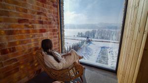 Eine Frau sitzt in einem Korbsessel und schaut aus dem Fenster in der Unterkunft Czorsztyn Prestige Apartamenty in Czorsztyn